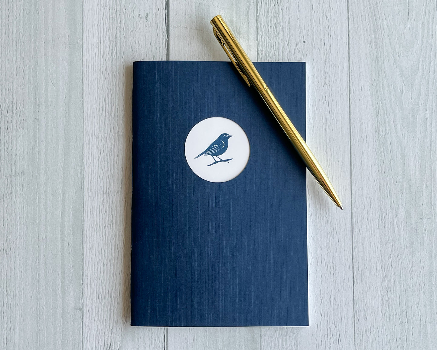 Signature Mini handbound journal in Midnight blue linen-textured cardstock with circular logo window.