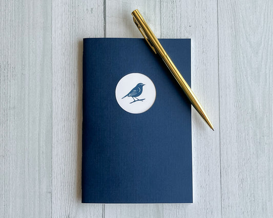 Signature Mini handbound journal in Midnight blue linen-textured cardstock with circular logo window.